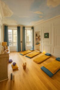 Salle de méditation lumineuse avec tapis au sol, plafond peint en ciel et nuages, dédiée aux soins et pratiques énergétiques.